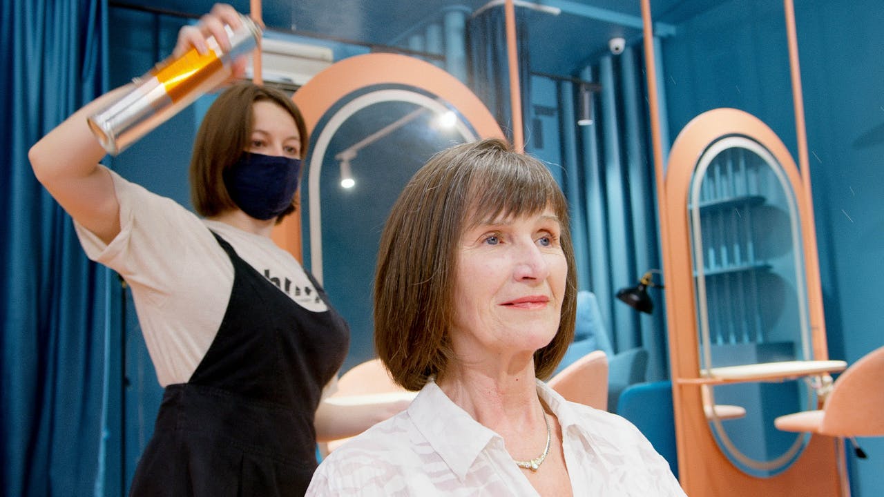 gallery-01 A hairstylist applies hairspray to a senior woman's new hairstyle in a modern salon.